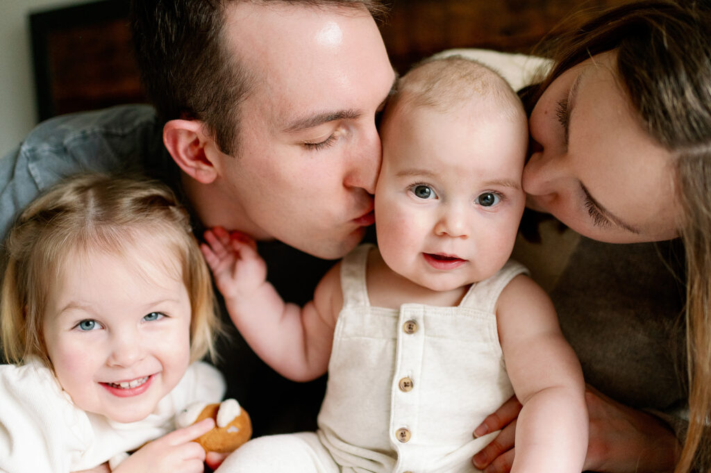 mom and dad kissing their baby boy on the cheeks, older sister smiles at the camera