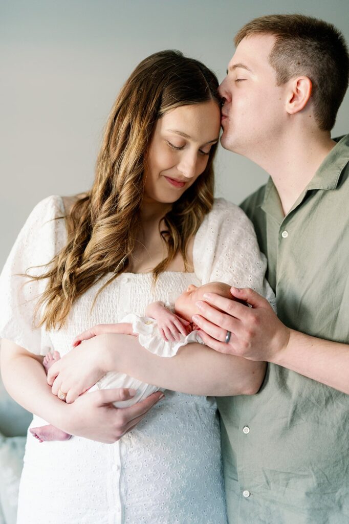 dad kissing mom who is looking at newborn at their in-home newborn session