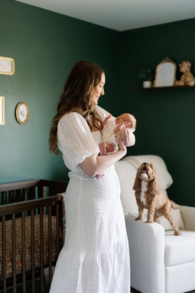 Mom holding newborn baby with dog looking at their in home newborn lifestyle session