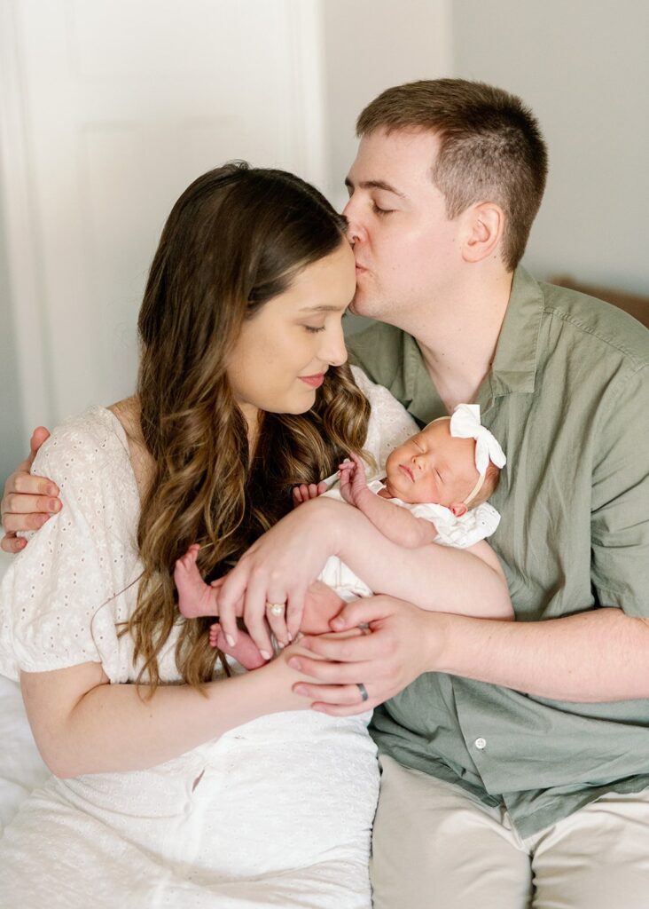 new parents kissing and holding newborn baby at in home newborn lifestyle session