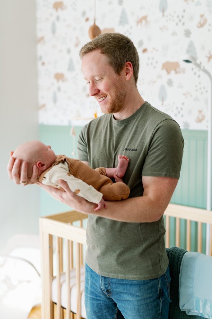 dad looking at newborn baby near crib at in-home newborn session MN