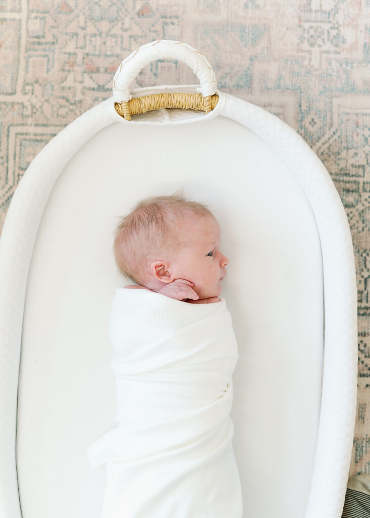 When Is the Best Time to Take Newborn Photos | Bauer Creative Baby lies in white swaddle in white bassinet, answering the question of when Is the best time to take newborn photos.