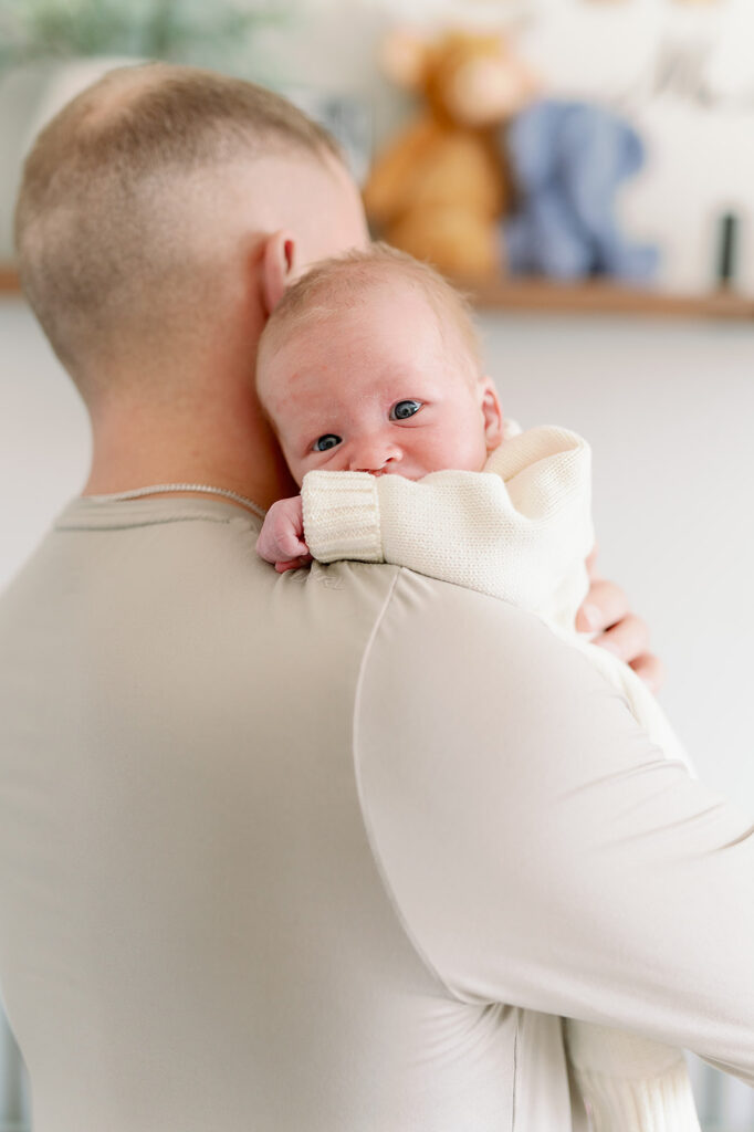 When to Take Newborn Photos | Bauer Creative When to take newborn photos for a cozy in home newborn session. Newborn stares over dad's shoulder, looking right at the camera.