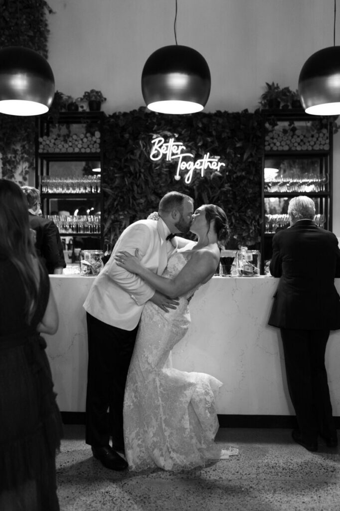 Wedding photographers in Minneapolis capturing a couple kissing at their reception bar under soft lighting. 