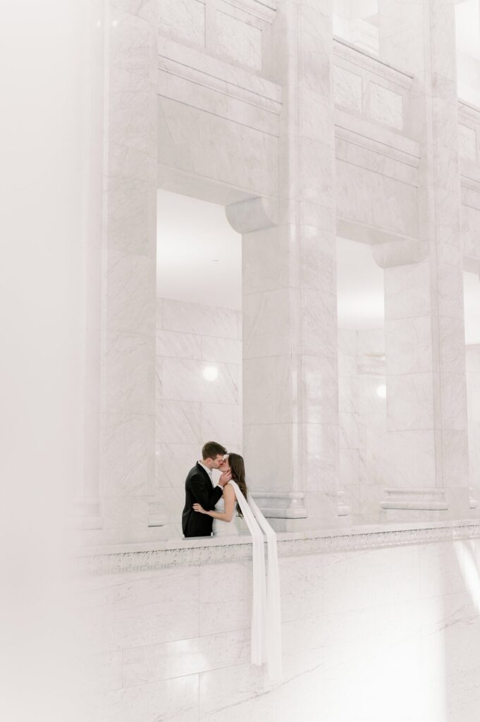 A couple kissing inside a bright marble venue with tall columns, by Minneapolis wedding photographer.