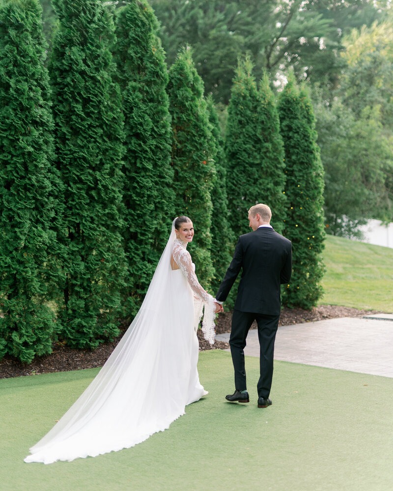 A wedding photographer in Minneapolis, MN capturing a bride and groom walking hand in hand along a tree-lined path. 