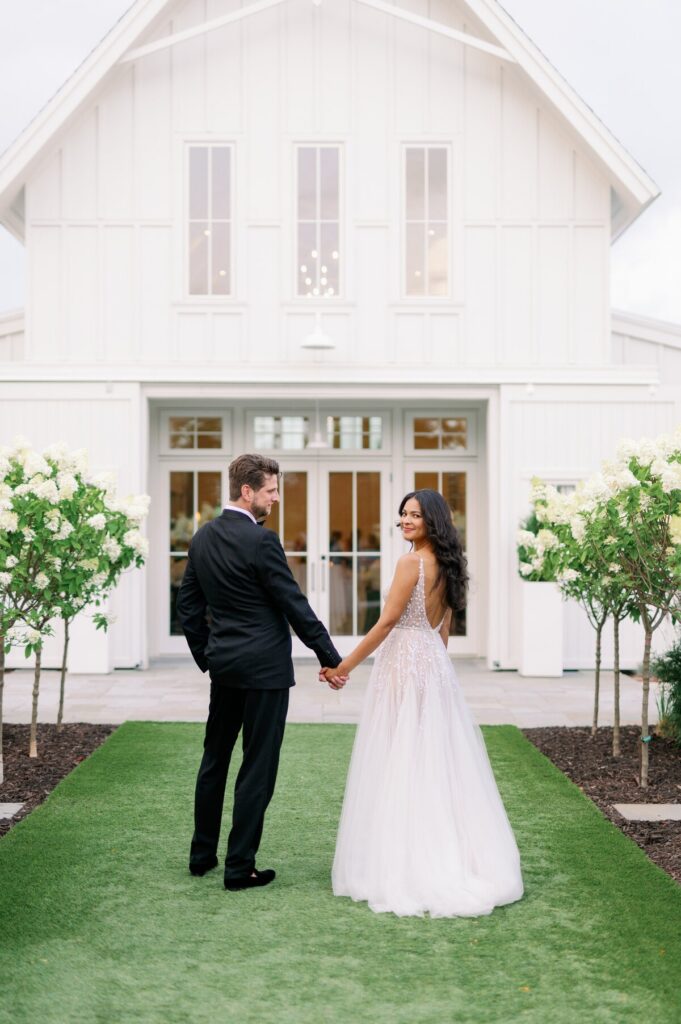 Wedding photographers in Minneapolis capture a bride and groom walking hand in hand outside a white wedding venue. 
