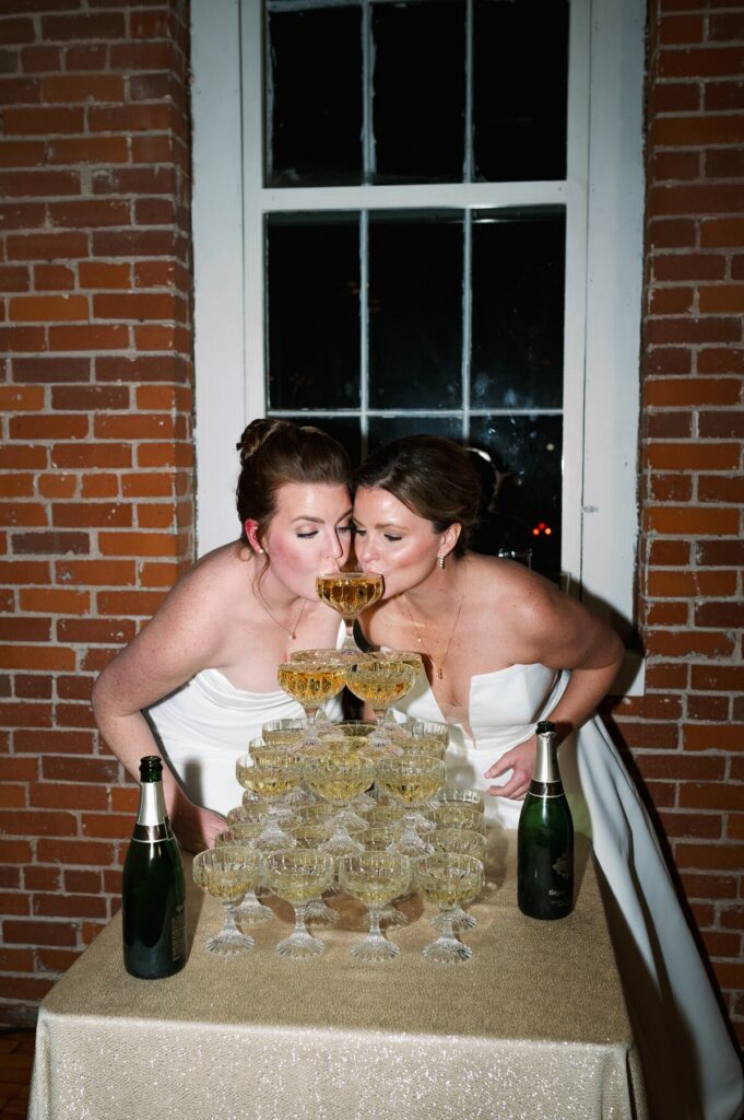 Wedding photographers in MN capturing two brides celebrating with a champagne tower during their reception. 