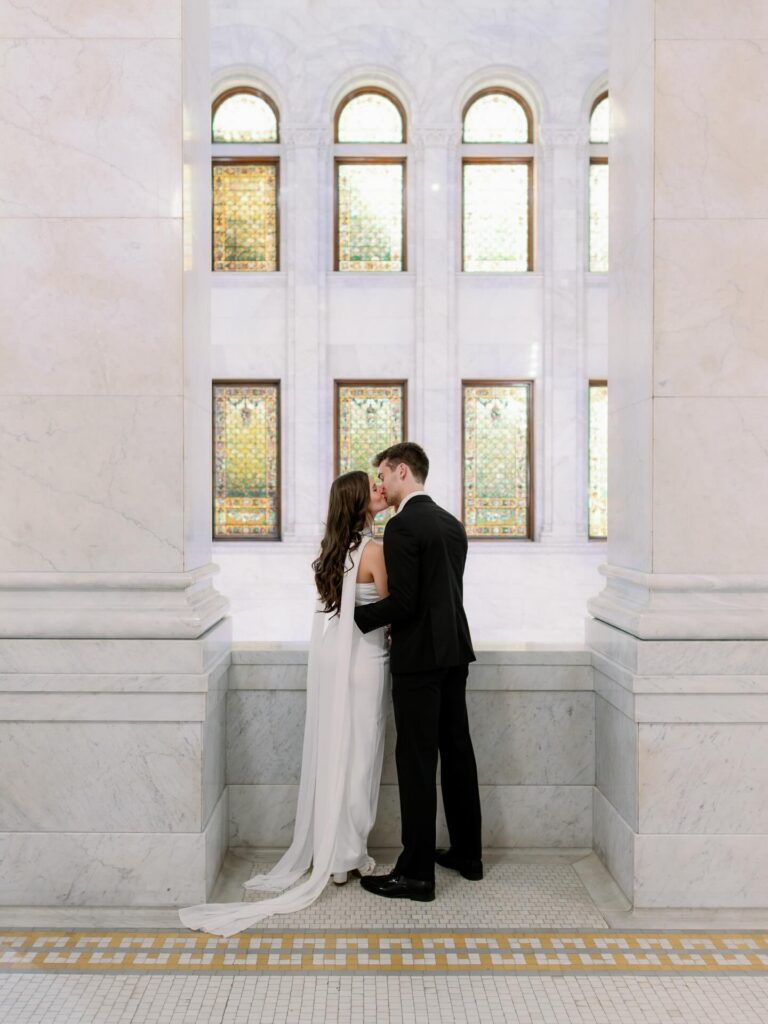 A couple sharing a kiss inside a bright, elegant space with stained glass windows, captured by wedding photographer in MN. 